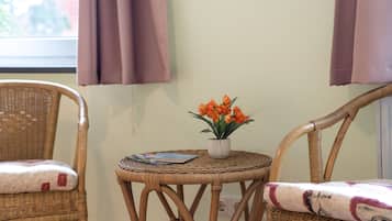 Ein Zimmer mit zwei Korbstühlen, einem kleinen Tisch mit Blumentopf und einem fenster mit Vorhängen.