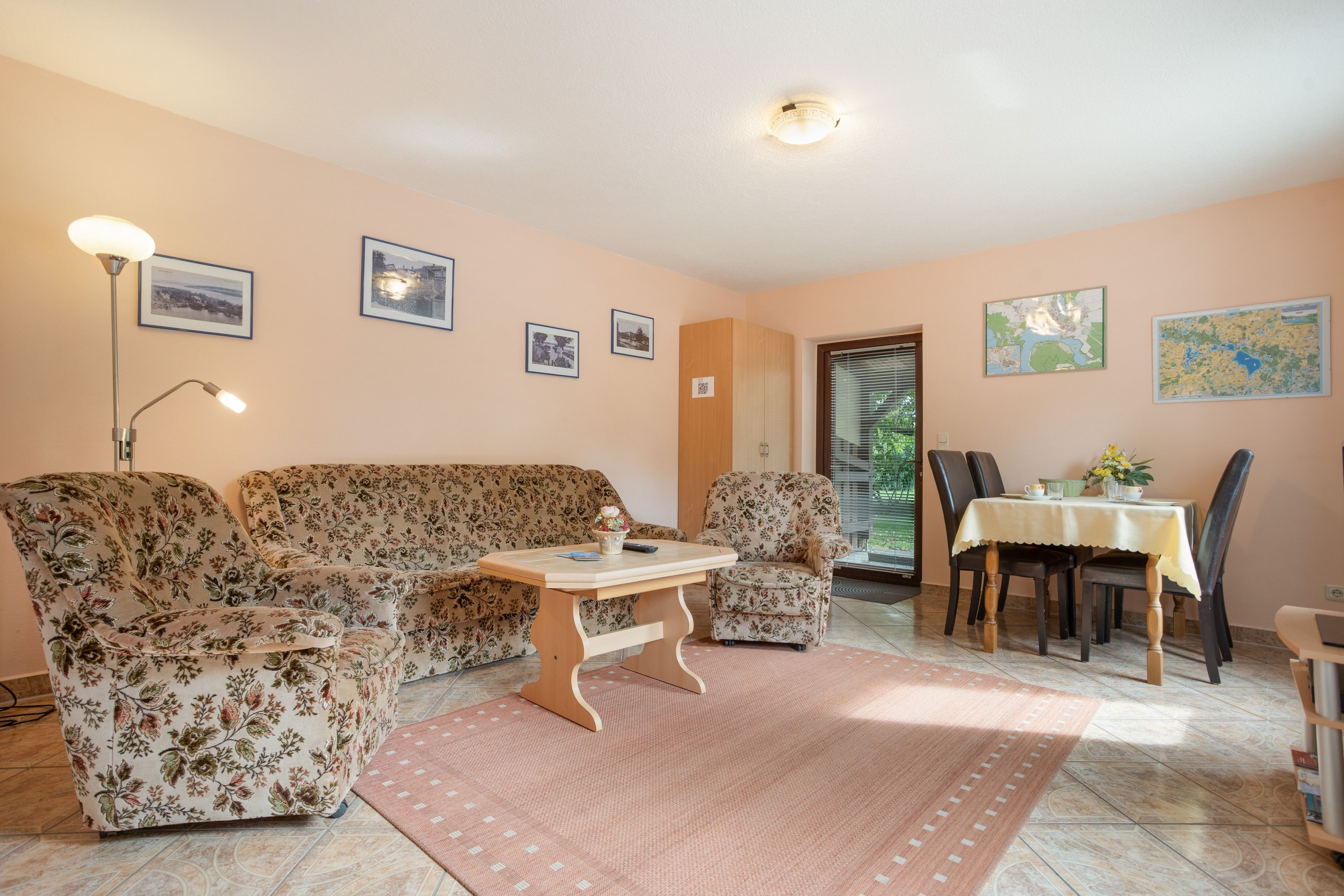 Una sala de estar con un sofá floral, una mesa de centro de madera y un comedor con mesa y sillas.