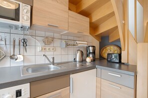 Een moderne keuken met een inbouwmagnetron, een roestvrijstalen spoelbak en houten keukenkastjes.