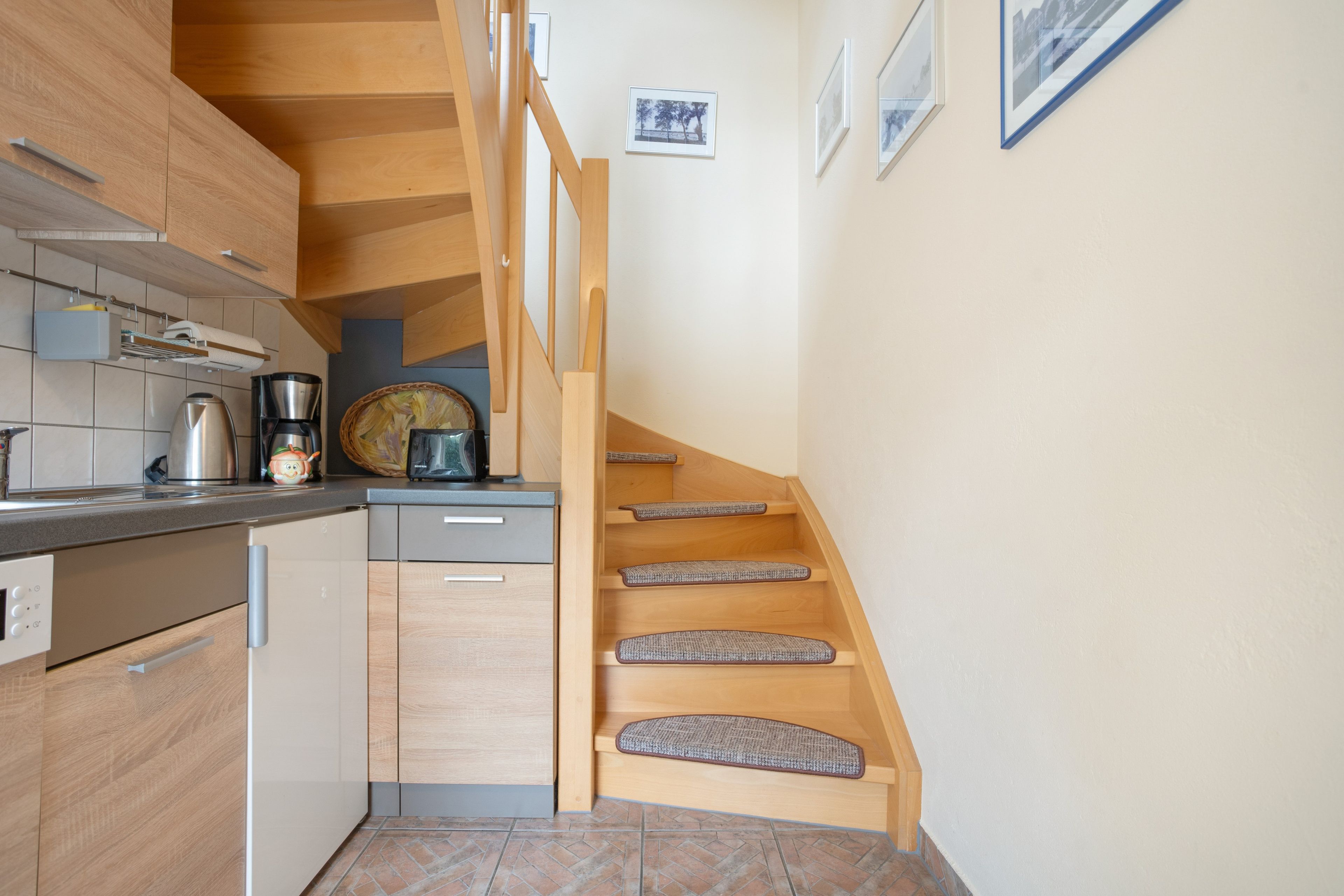A kitchen with wooden cabinets, a coffee machine, and a staircase with cushioned steps.