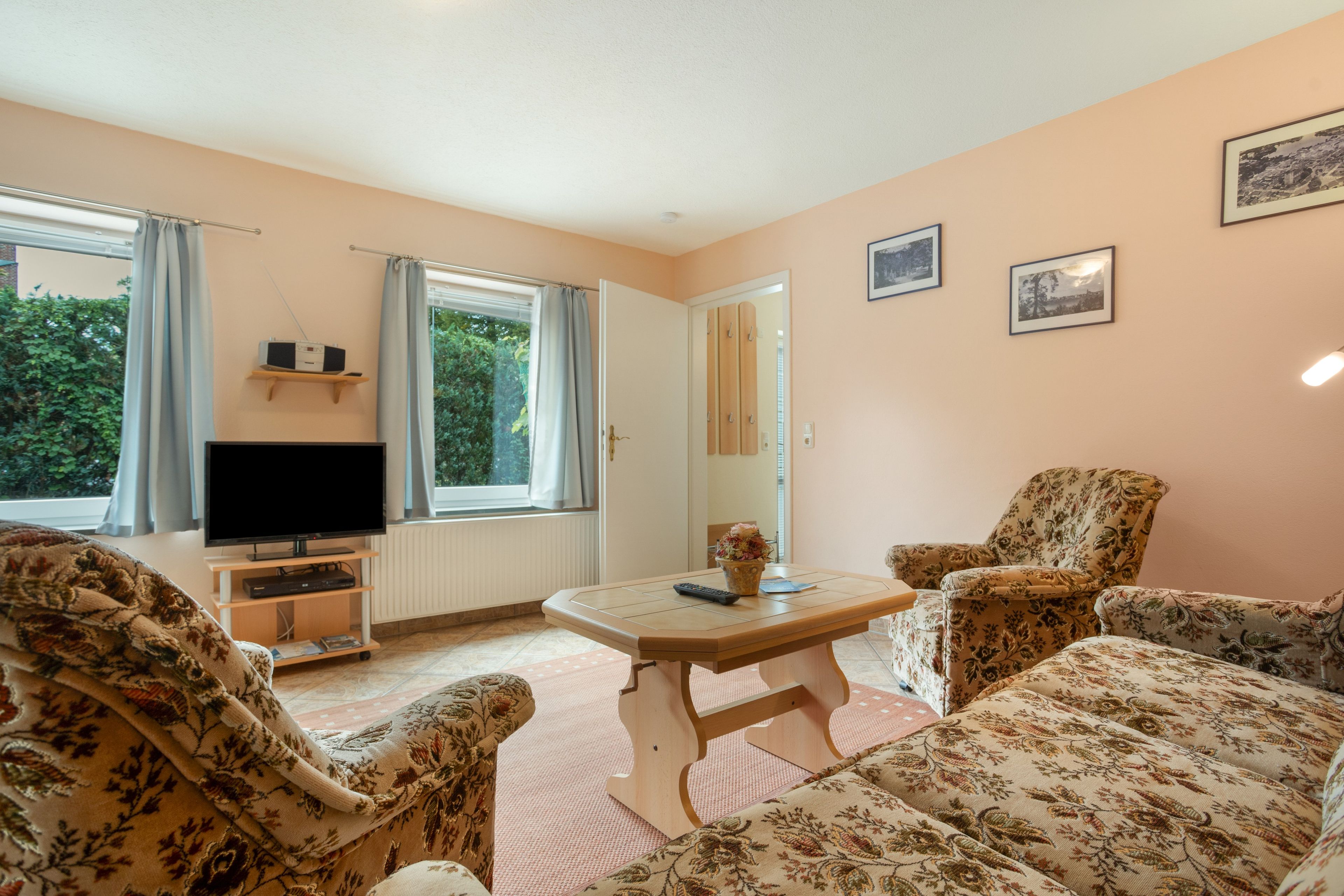 Ein Wohnzimmer mit Fernseher, einem Tisch und zwei gemusterten Sesseln.