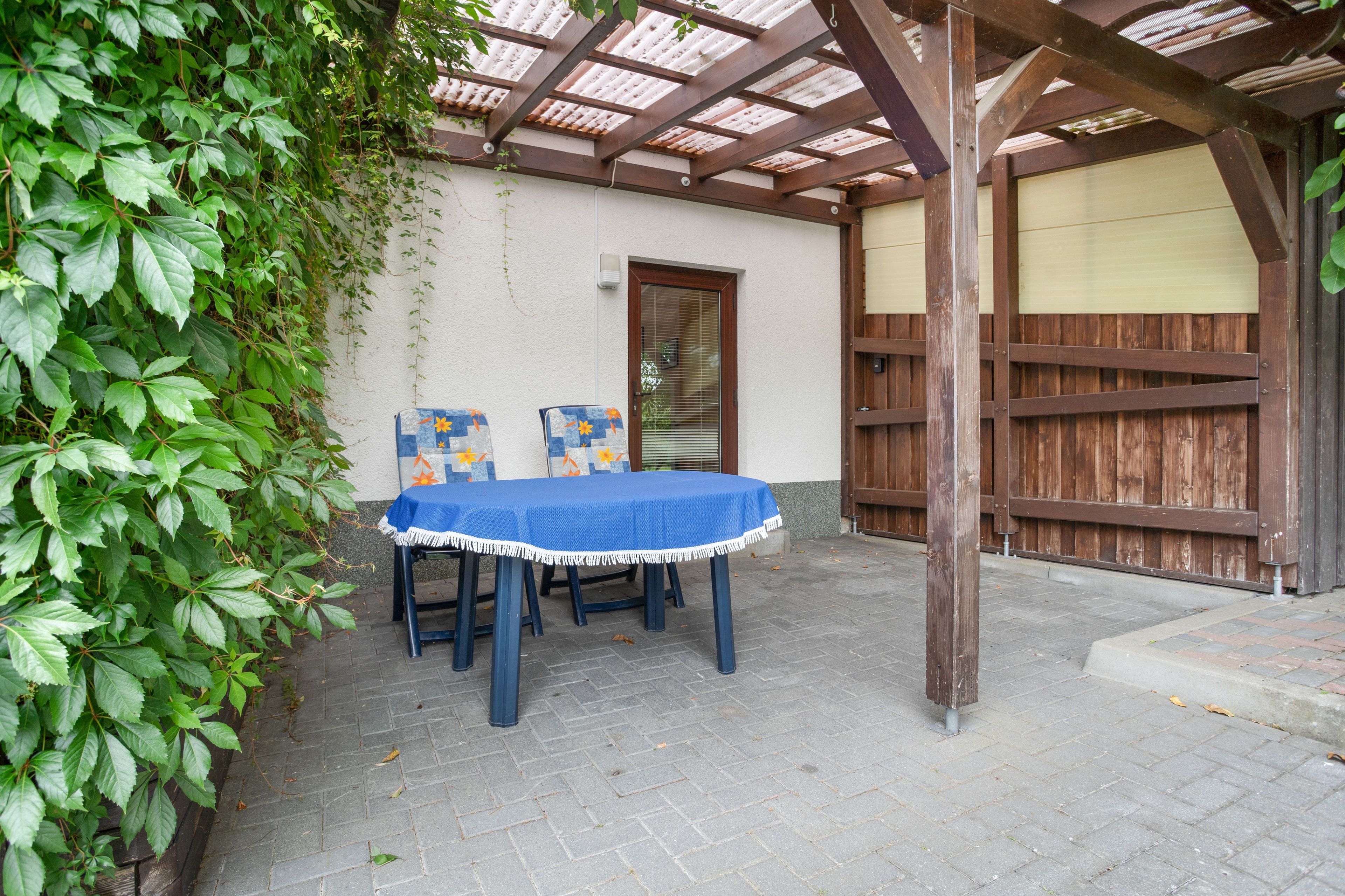Eine Terrasse im Freien mit Tisch und Stühlen, einer Holzwolyleiter und einer Mauer mit einer Tür.