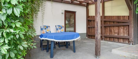 An outdoor patio with a table and chairs, a wooden pergola, and a wall with a door.