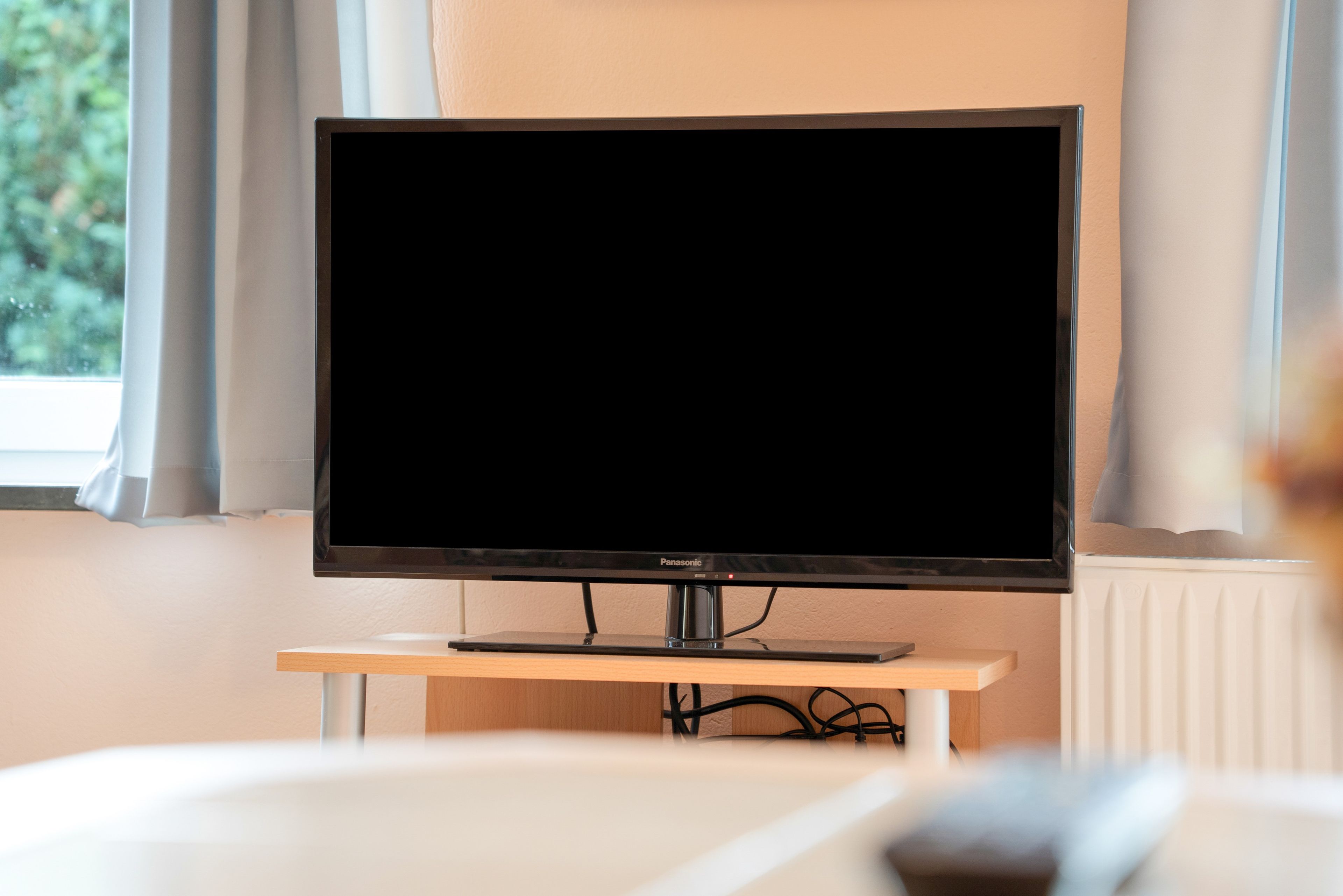 A television on a stand in a room with a window and curtains.