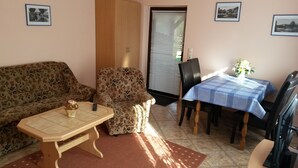 Un salon comprenant un canapé, une petite table, une table à manger avec des chaises et une fenêtre avec des stores.