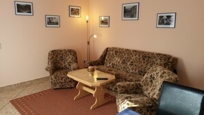 Un salon avec un canapé à motifs floraux, deux fauteuils, une table basse en bois et un lampadaire.