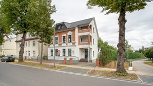 Ein mehrstöckiges Wohngebäude mit Backsteinfassade, einem verschlossenen Eingangsbereich und einem Parkplatz mit einem Auto.
