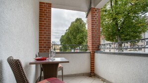 Ein Balkon mit Tisch und Stühlen, einem roten Kissen und Blick auf Bäume und Gebäude.