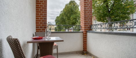 Un balcon avec une table et des chaises, un coussin rouge et une vue sur les arbres et les bâtiments.