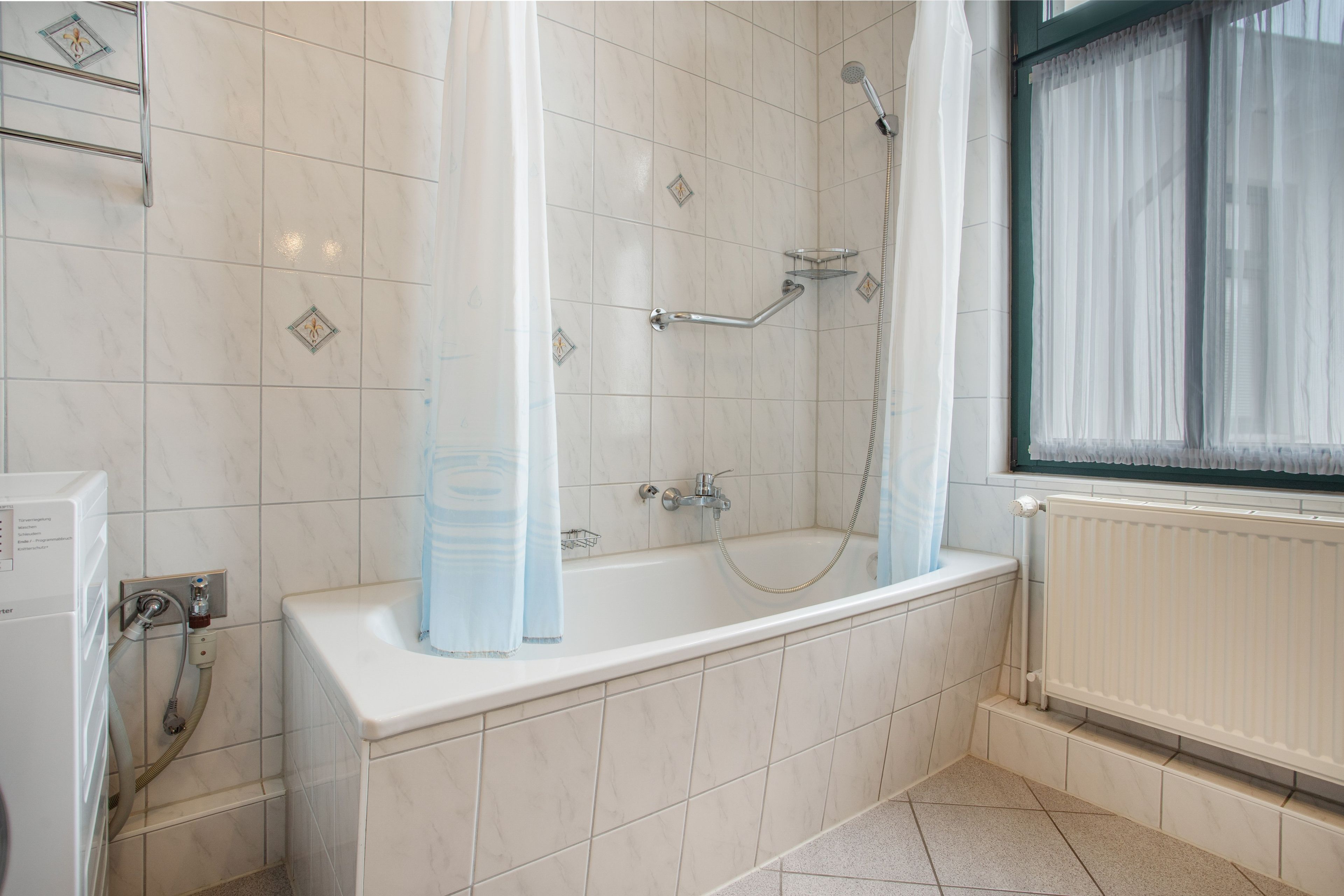 Ein Badezimmer mit Badewanne, Dusche und einem Fenster mit Vorhängen.