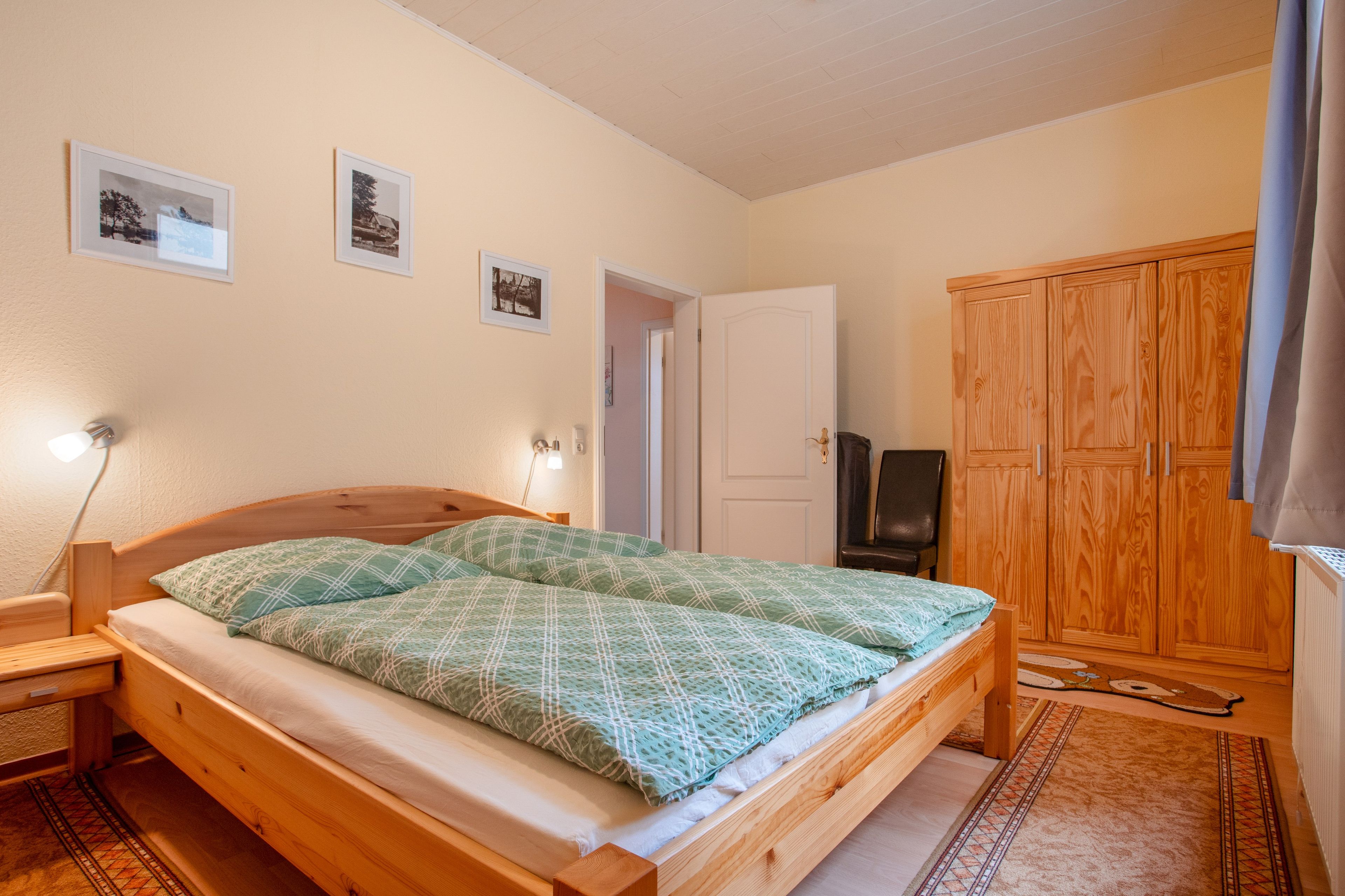Ein Schlafzimmer mit einem hölzernen Bett, einem Nachttisch, einem Kleiderschrank und drei gerahmten Bildern an der Wand.
