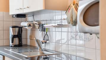 Eine moderne Küche mit einer Edelstahl-Spüle, einer Kaffeemaschine und einem Hängegestell mit Küchenutensilien.