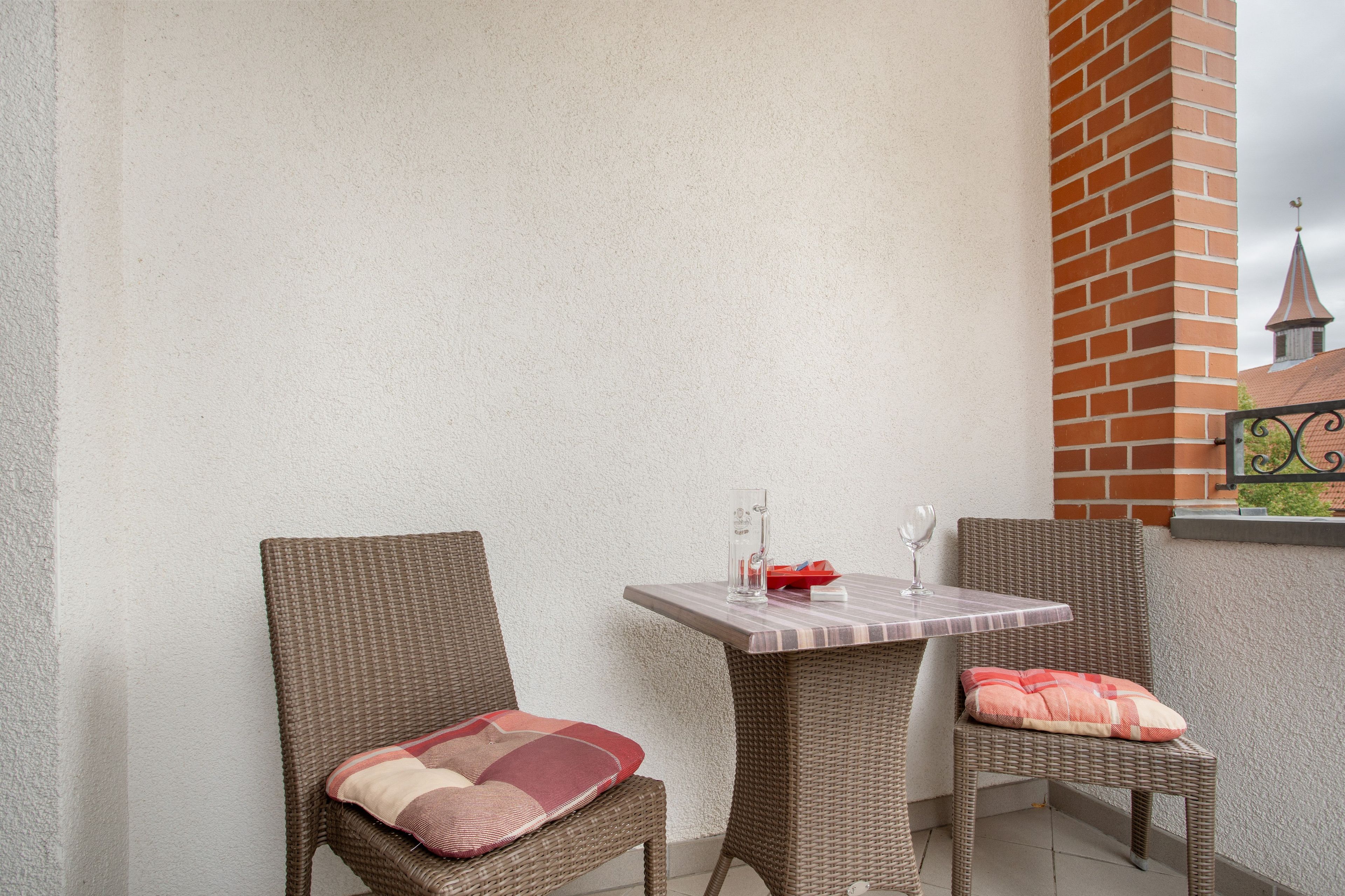 Eine Ecke eines Raumes mit einem Korbstuhl, einem Tisch mit einem Glas und einer Backsteinwand.