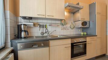 A modern kitchen with light wood cabinets, a stainless steel range hood, a built-in oven, and a coffee maker.