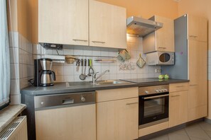 Une cuisine moderne avec des meubles en bois clair, une hotte de cuisine en acier inoxydable, un four encastré et une machine à café.