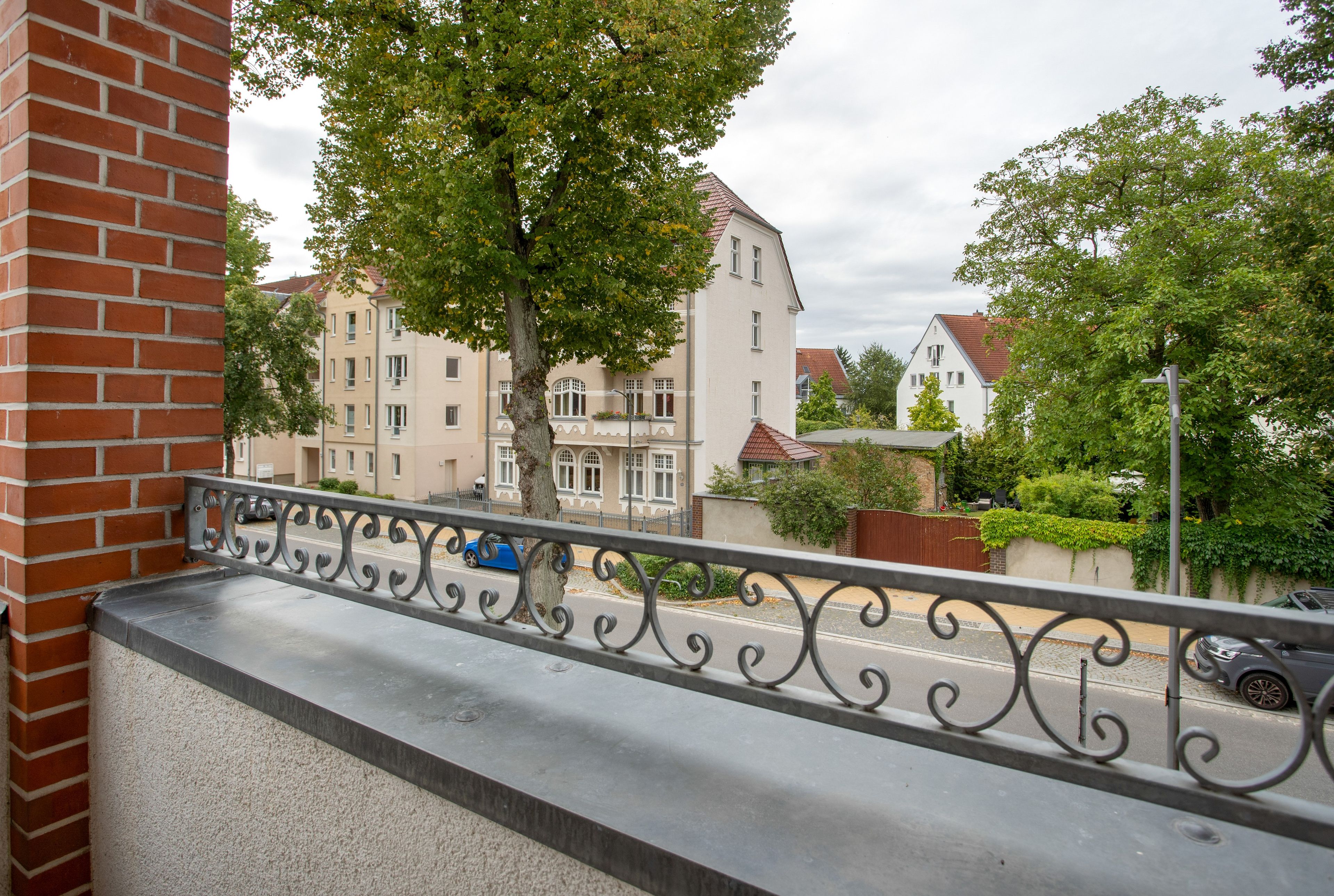 Ein Balkon mit schmiedeeisernem Geländer mit Blick auf eine Straße, gesäumt von Gebäuden und Bäumen.