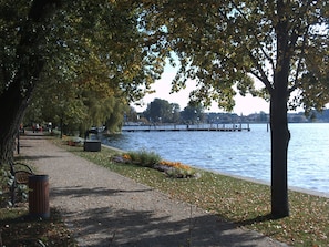 A lakeside park with a walking path, benches, and a statue.