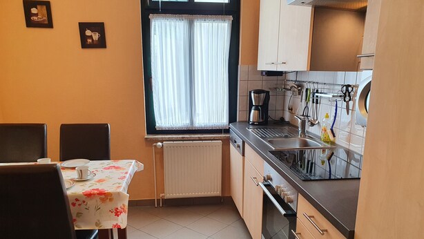 A compact kitchen with a dining table, chairs, a window with curtains, and basic appliances.
