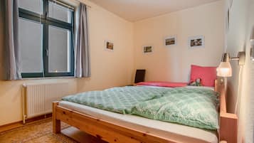 A bedroom with a single bed, a window with curtains, a radiator, and a wall with three framed pictures.