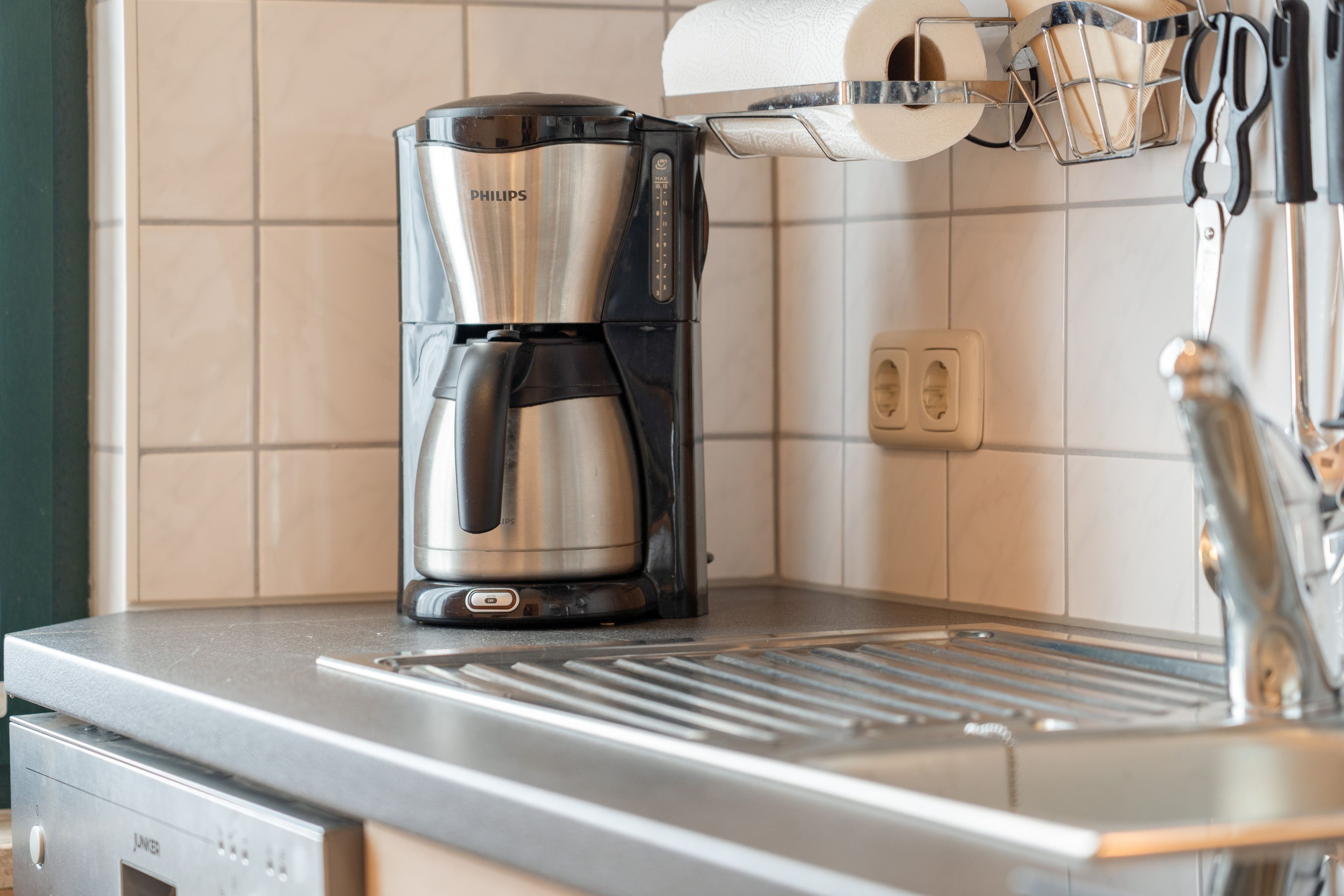 A kitchen with a coffee maker, a paper towel holder, and a sink.