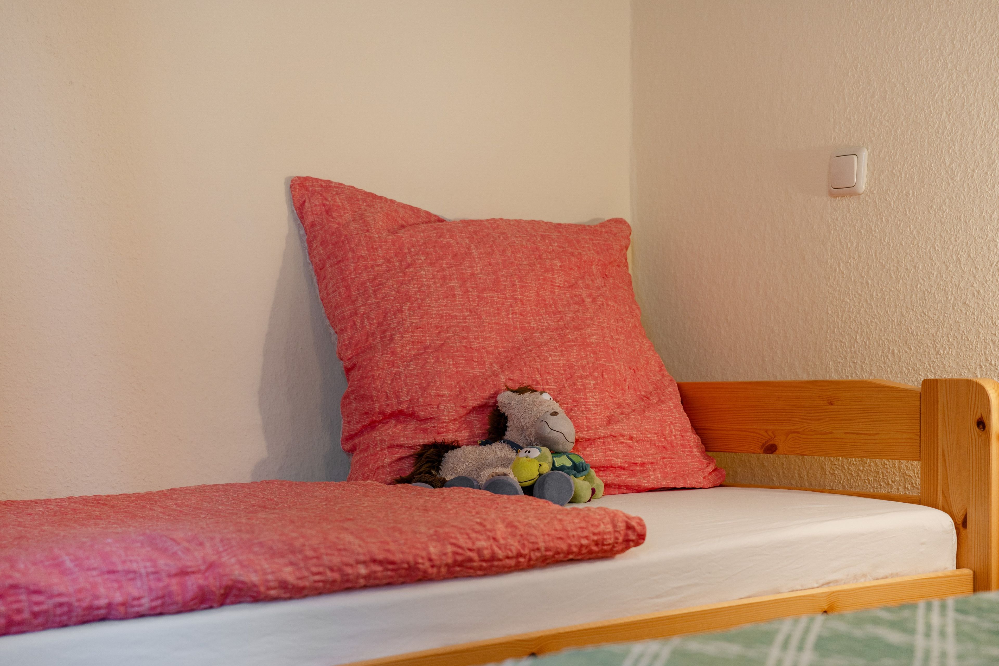 Ein Einzelbett mit Holzrahmen, einer weißen Matratze und einer roten Decke.