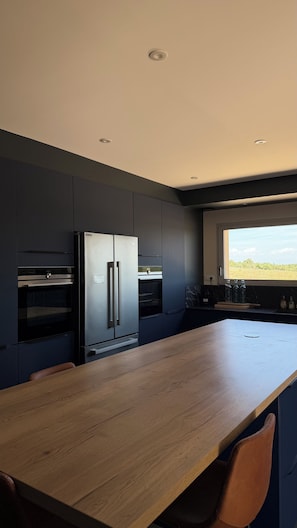 Eine moderne Küche mit dunklen Schränken, einem Edelstahlkühlschrank und einem Holztisch.