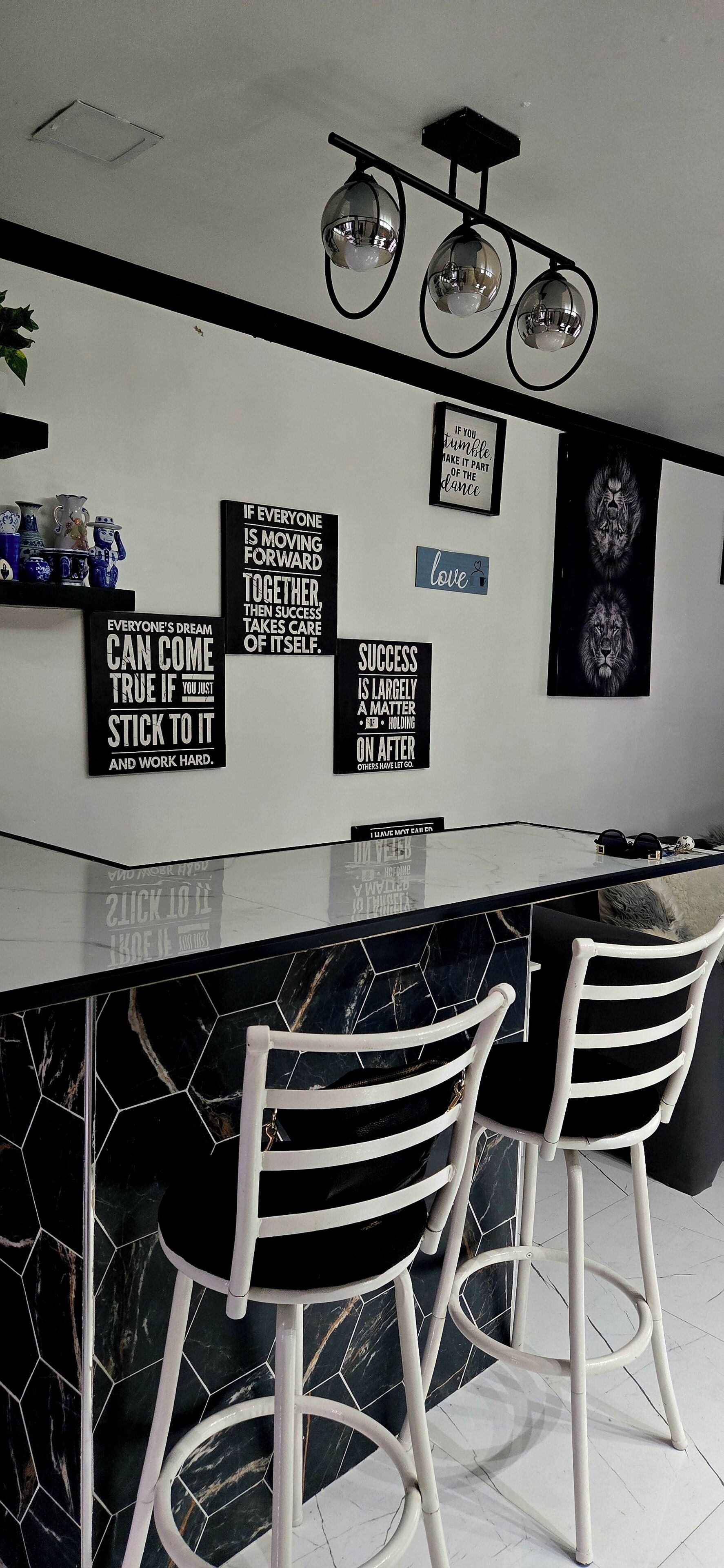 A modern kitchen with a black and white marble backsplash, two white bar stools, and motivational wall art.