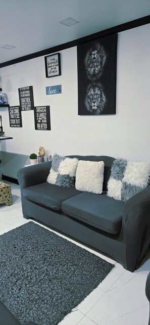 Ein modernes Wohnzimmer mit grauem Sofa, flauschigen Kissen, einem grauen Teppich und motivierenden Wandbildern.