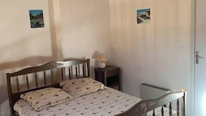 A bedroom with a wooden bed, a bedside table with a lamp, and two small wall-mounted pictures. - Mountain views and comfort near Barcelonnette (Enchastrayes)