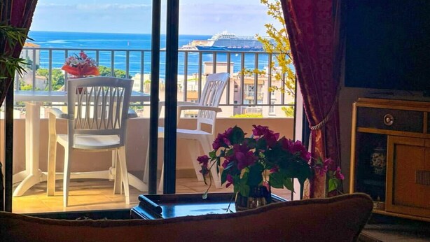 En balkong med utsikt över havet, en stol, ett bord och en vas med blommor.