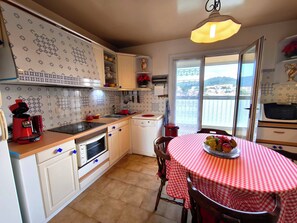A kitchen with a red and white checkered tablecloth, a coffee maker, and a view of the sea through the window. - Large, bright apartment with balcony and sea view (Ajaccio)