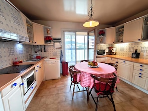 A kitchen with a dining table, chairs, a microwave, and a sink. - Large, bright apartment with balcony and sea view (Ajaccio)