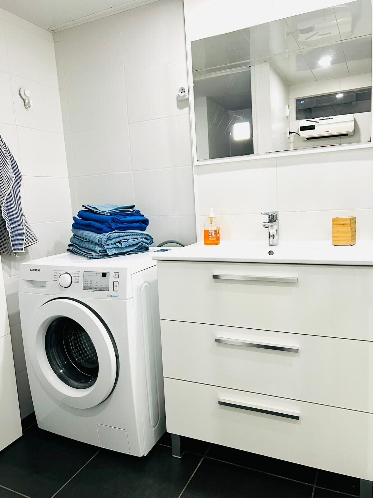 A modern laundry room with a Samsung washing machine, a sink, and a mirror above it.