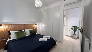 Ein Schlafzimmer mit Bett, Nachttischen, einem Holz-Kopfteil, einer Hängeleuchte, einem Kleiderschrank und einer Topfpflanze.