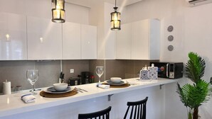 Een moderne keuken met witte kastjes, een aanrecht, twee hangende hanglampen, een magnetron en een potplant.