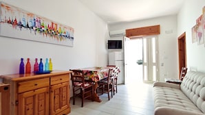 Un comedor con una mesa y sillas, un sofá, un aparador, botellas de colores, un televisor y un equipo de aire acondicionado.