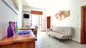 Una sala de estar con un sofá, una mesa de madera con botellas de colores, un televisor y un refrigerador.