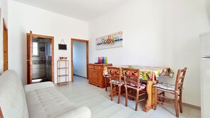 Ein Wohnzimmer mit einer Couch, einem Esstisch mit Stühlen, einem Holzschrank und einem Wandbild.