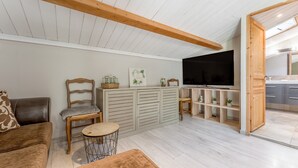 Una sala de estar con un sofá, una silla, una mesita redonda, un televisor y un mueble de madera con estantes.