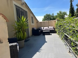 Een terras buiten met een bank, een grote potplant en een rieten mand.