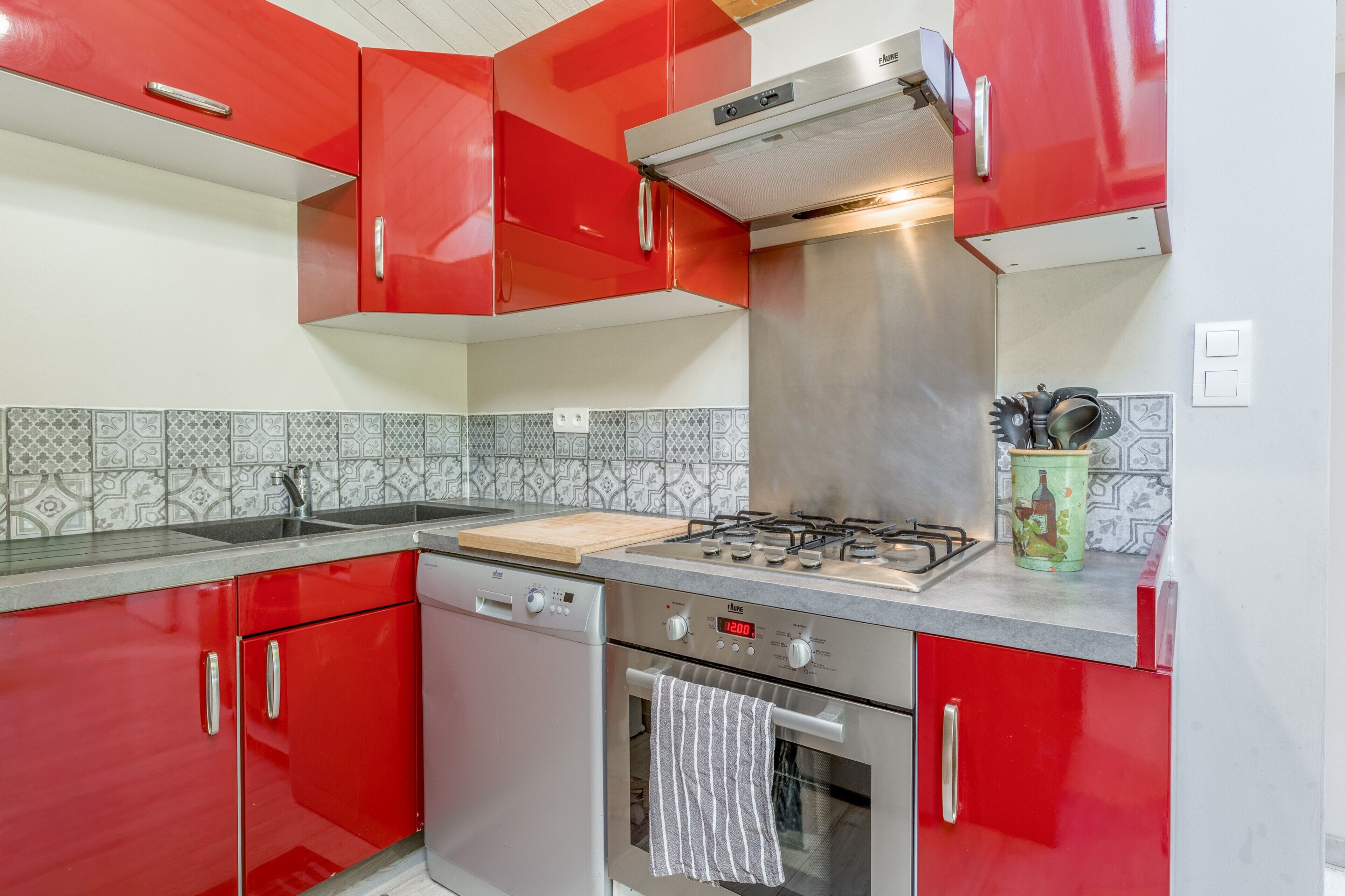 A kitchen with red cabinets, a gas stove, a dishwasher, and a tiled backsplash.