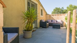 Un patio con mobiliario de mimbre, una planta en maceta y un edificio con pared beige y ventanas.