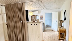 A room with a wooden floor, a beige rug, a white cabinet with hooks, a hanging light fixture, and a door leading to another room. - Rural charm and modern comfort – close to nature and swimming |SE08016 (Ljung)