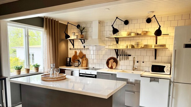A modern kitchen with a central island, white cabinetry, a microwave, and a refrigerator. - Rural charm and modern comfort – close to nature and swimming |SE08016 (Ljung)