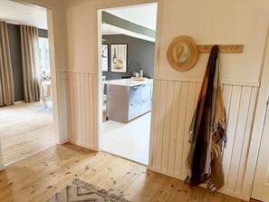 A room with wooden flooring, a dining area with a table and chairs, a kitchen with a counter and cabinets, and a hat hanging on the wall. - Rural charm and modern comfort – close to nature and swimming |SE08016 (Ljung)