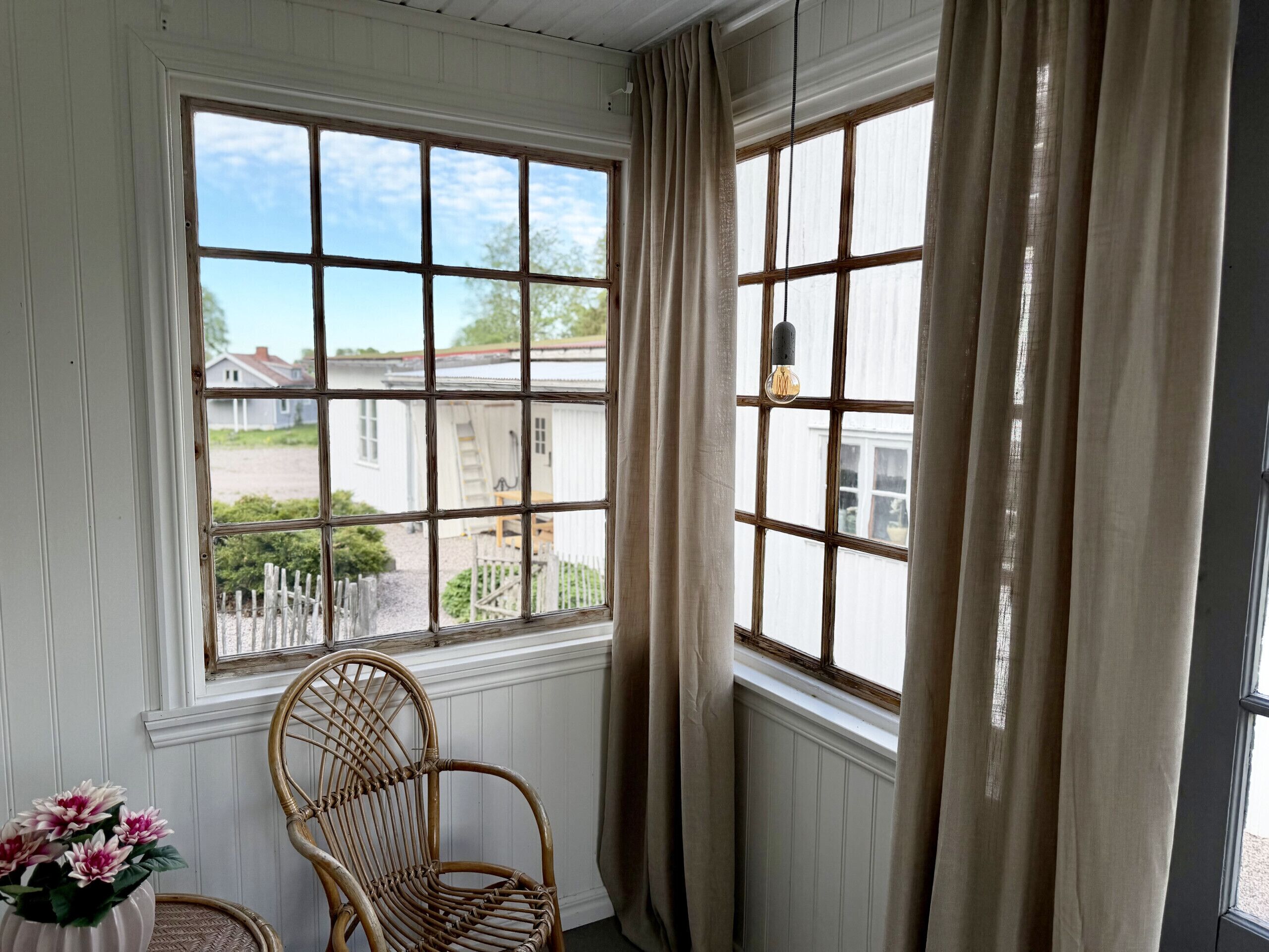 A room with a large window, a wicker chair, and a vase with flowers.