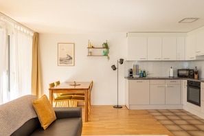 Un apartamento moderno con comedor, sofá, cocina con armarios blancos y una lámpara de pie.