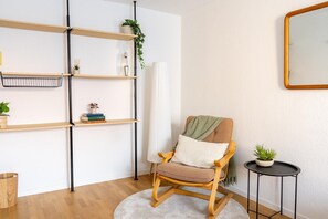 Una habitación con una mecedora de madera, una mesita auxiliar con una planta y un aparador con libros y objetos decorativos.