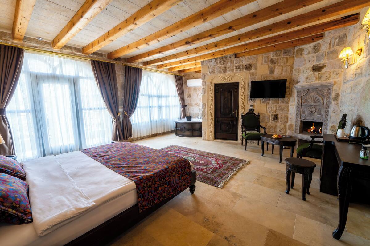 Quarto com cama, lareira, televisão e parede de pedra.