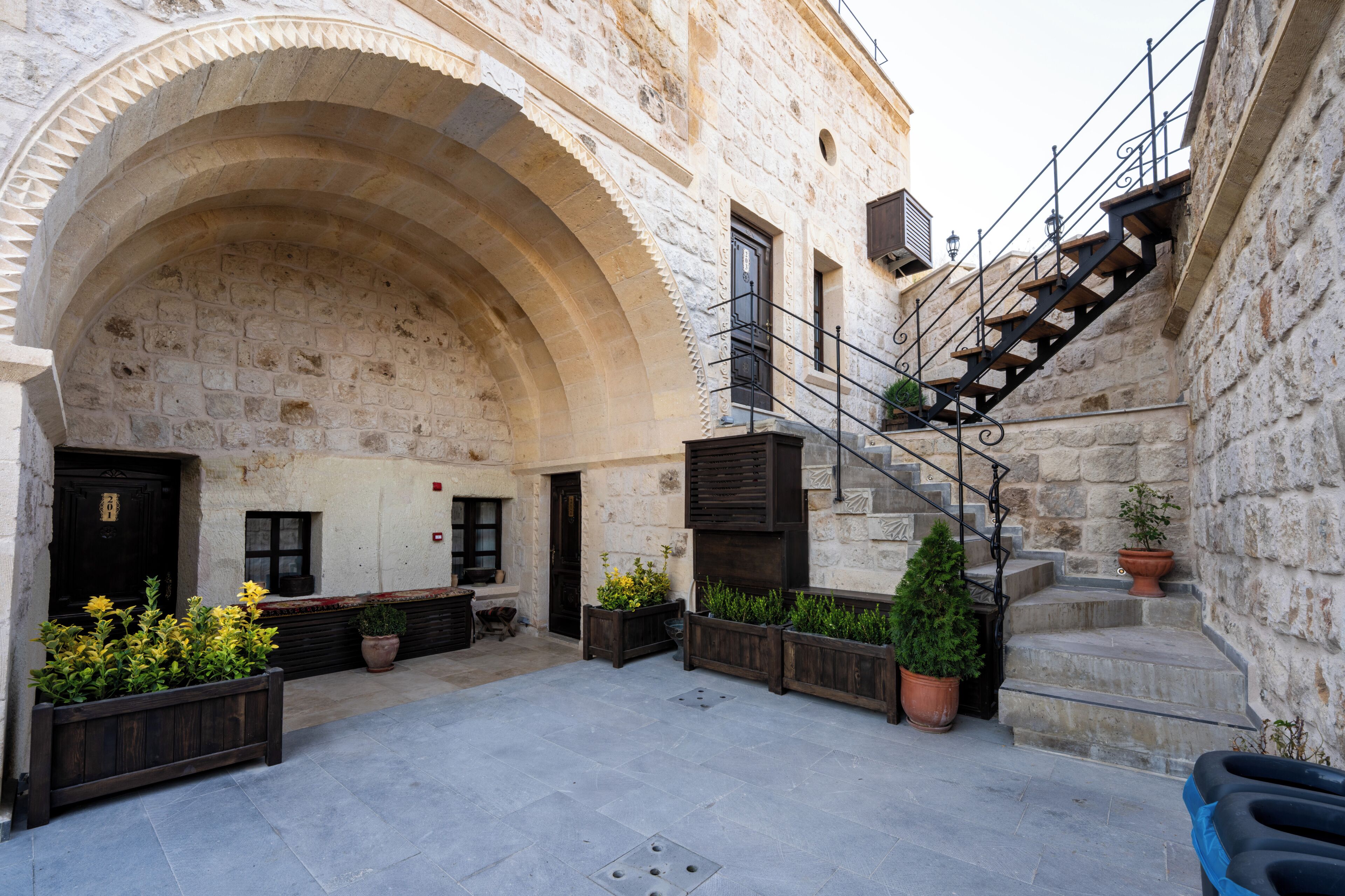 A courtyard with stone walls, a wooden bench, potted plants, and a staircase.